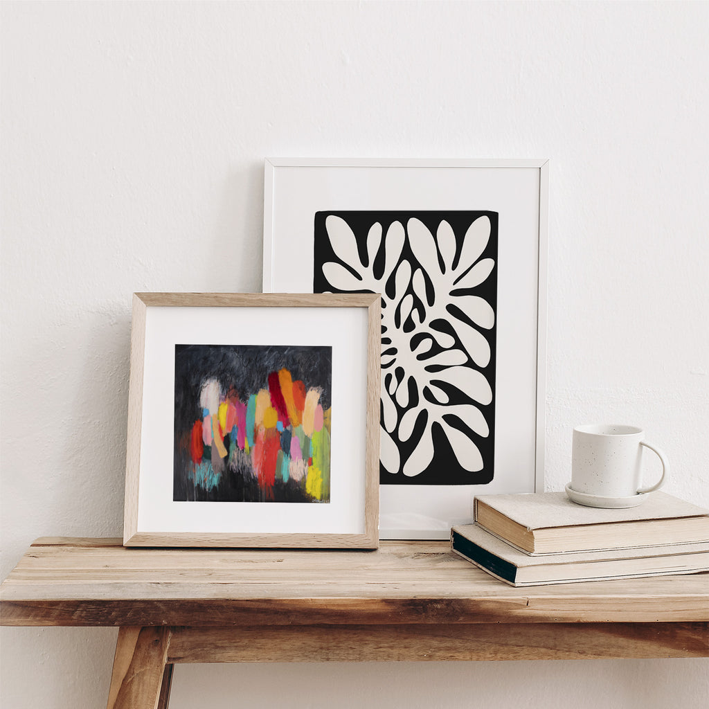 Two pieces of abstract wall art leaning against a wall on a desk.