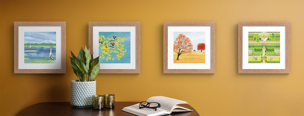 Nature art prints of trees, birds and greenery, hung up on an orange wall.
