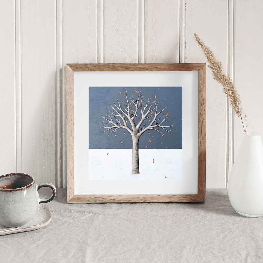 Stunning nature art print featuring a tree standing alone in the snow on a wintery landscape. Art print is leaning against a wall.