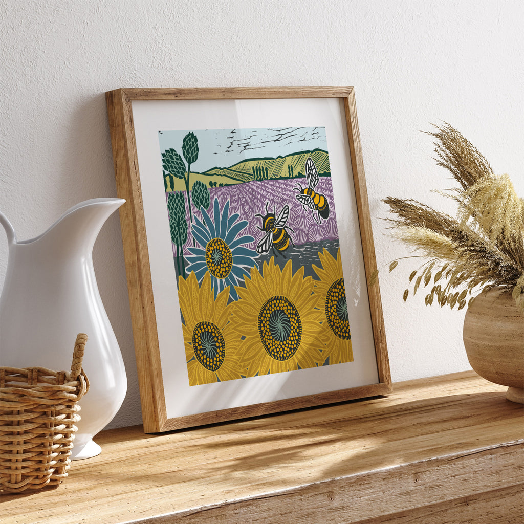 Nature art print featuring bees, sunflowers and fields of lavender. Art print is leaning on a table next to a jug.