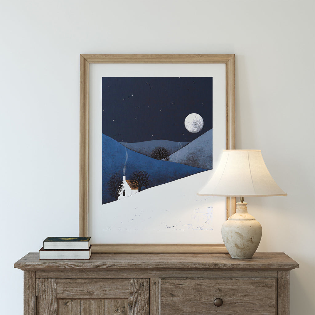 Stunning nature art print featuring a moon rising on a wintery landscape. Art print is leaning on a dresser against a white wall.