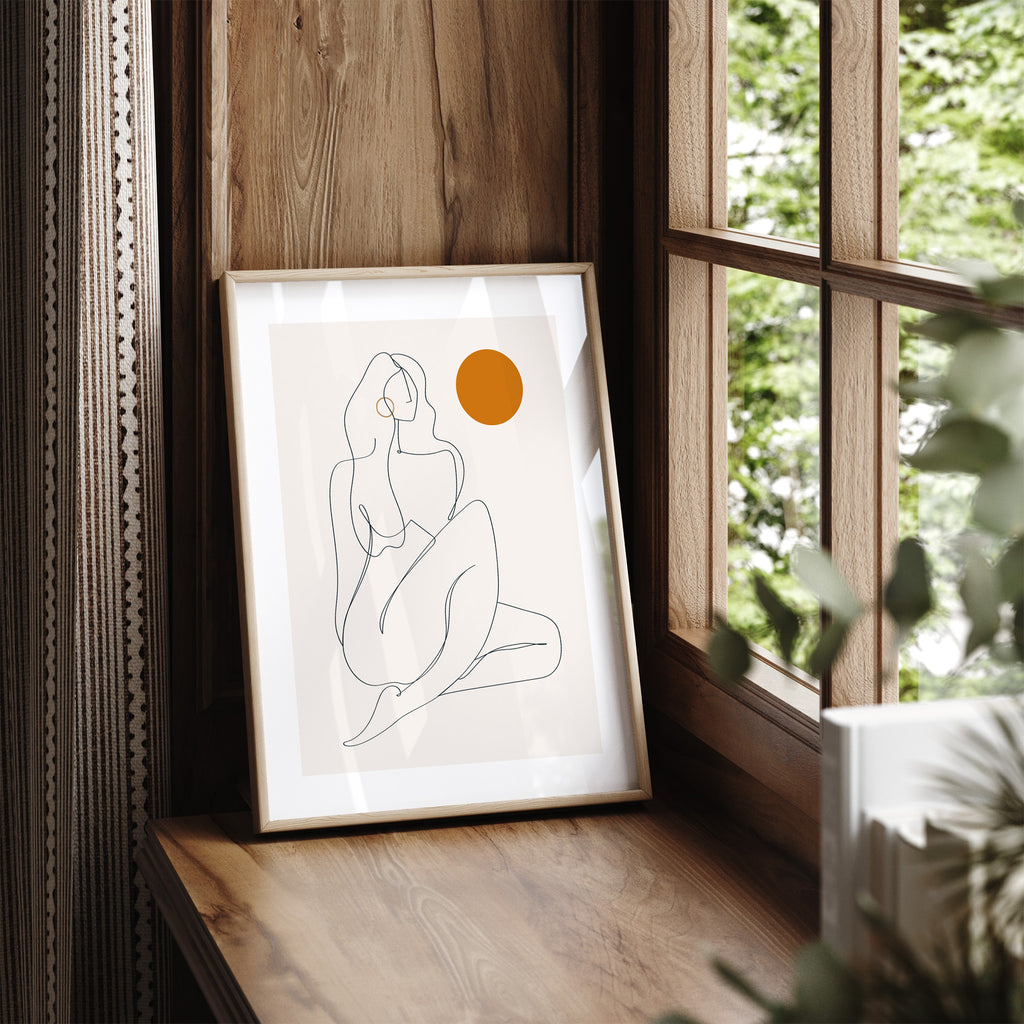 Art print containing clever line work creating the female form, accompanied by a splash of bright orange colour. Art print is framed and leaning on a window seat.