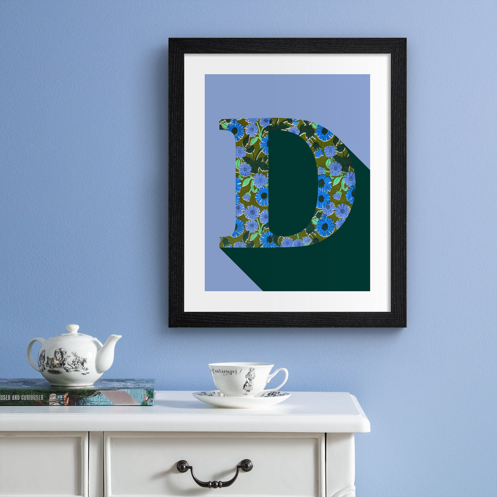 Alphabet art print of 'D' hung up on a blue wall.