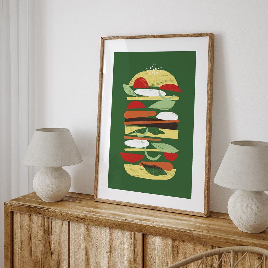 Bright art print featuring a minimalistic drawing of a burger, on a green background. Art print is leaning on a table against a wall.