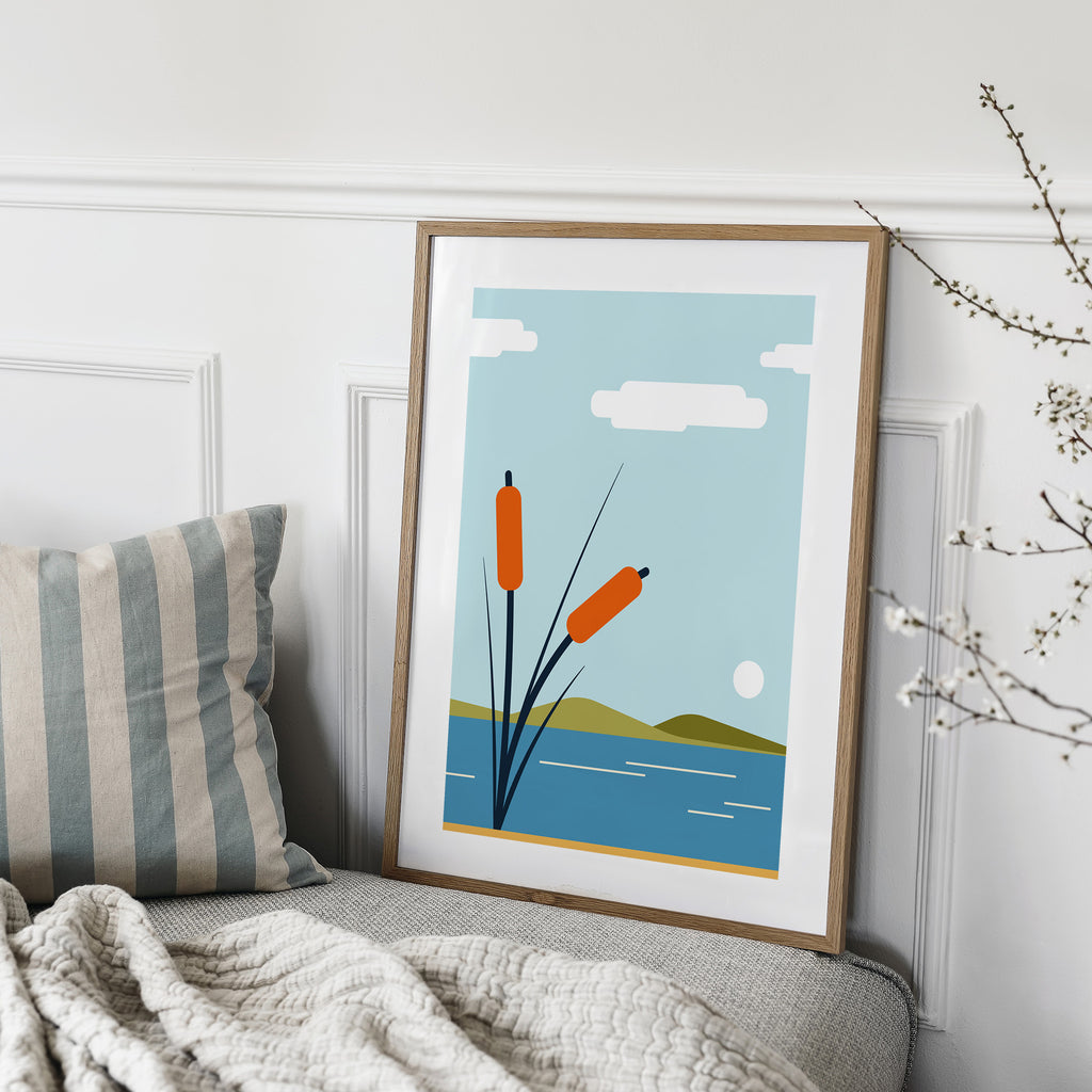 Minimalistic art print featuring bullrushes in front of a beautiful coast scene. Art print is on a sofa leaning against a wall.