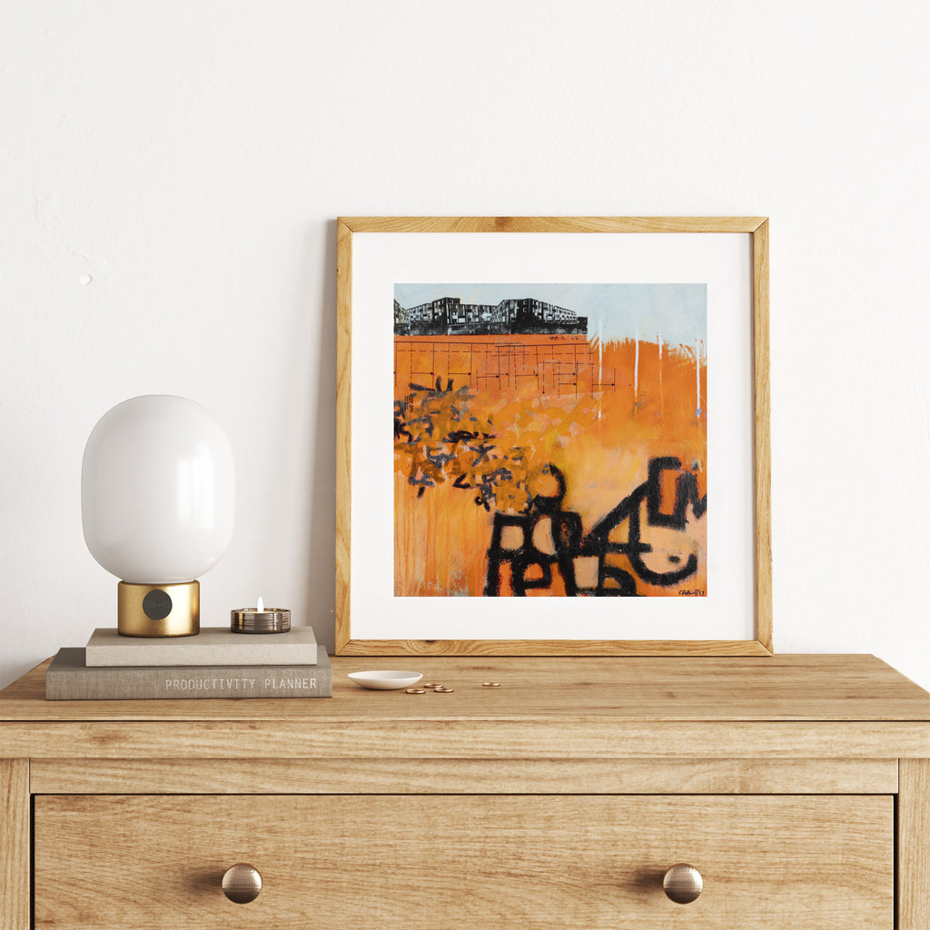 Vivid abstract print featuring an urban landscape covered in bright orange and black graffiti spray paint. Art print is on a chest of drawers.