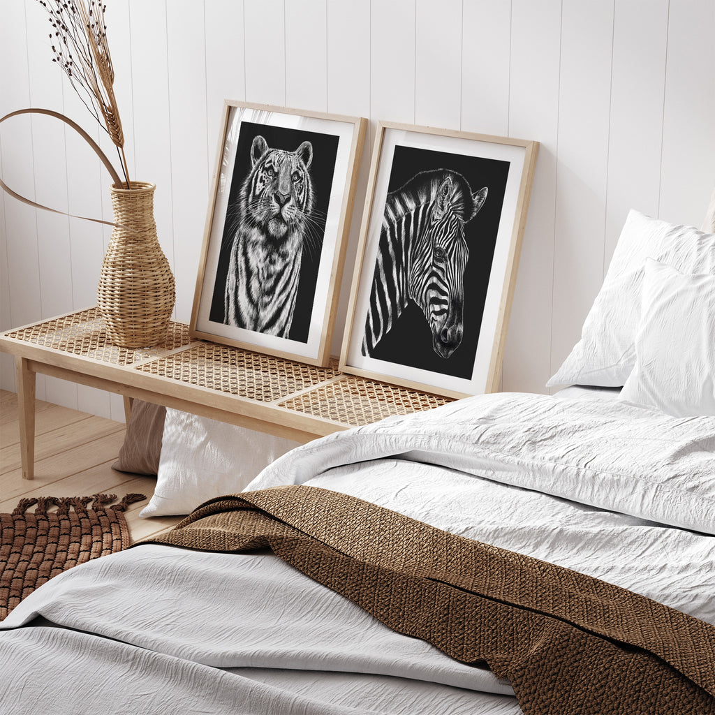 Striking art print featuring a detailed illustration of a tiger gazing upwards, in black and white. Art print is leaning against a wall next to a bed and another print.