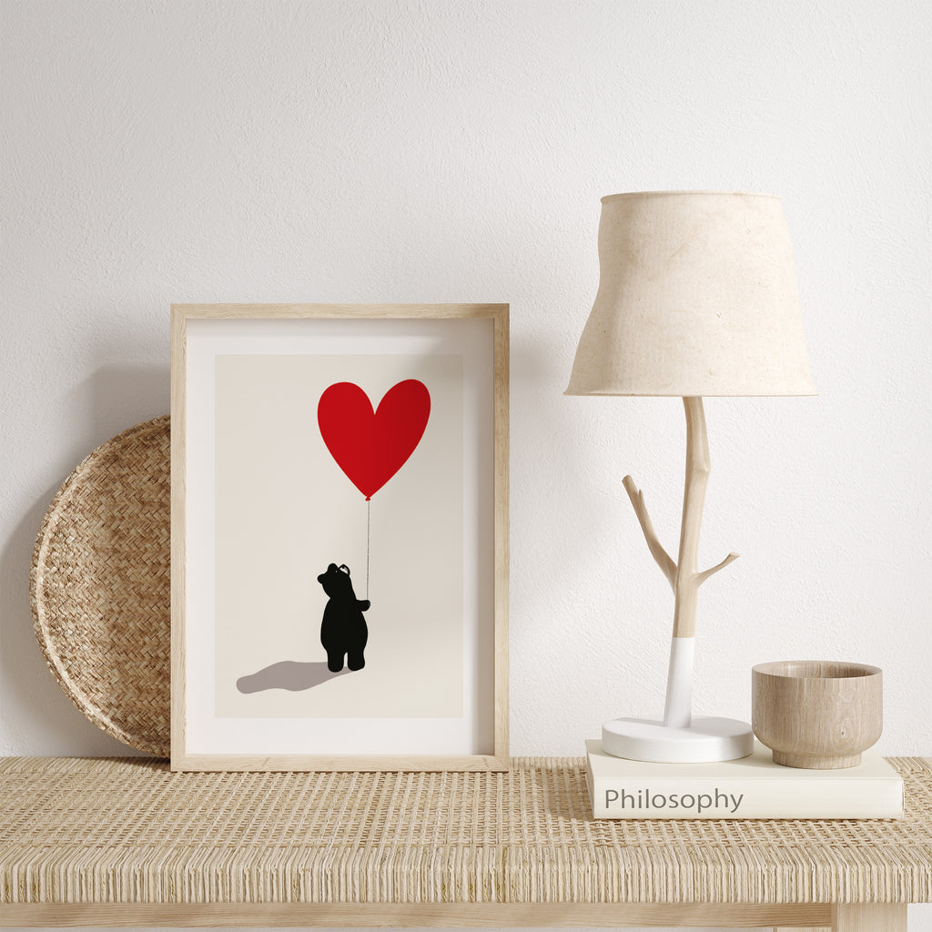 'Bear' art print of bear holding a bright red heart balloon. Art print is leaning against a white wall on a dresser.