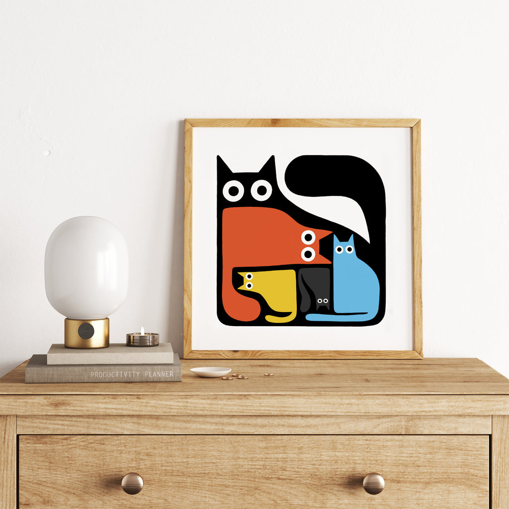 Colourful art print featuring a puzzle of colourful cats fitting inside a large black cat. Art print is leaning on a dresser.