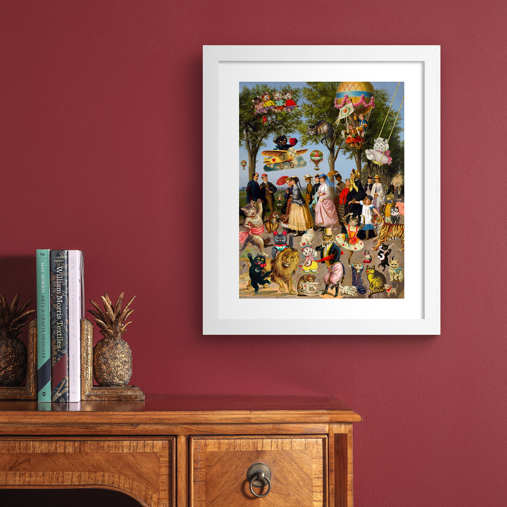 Stunning 'Pop-Surrealist' art print featuring a picnic spread of cats, people and playful characters on a bright summer day. Art print is hung up on a red wall.