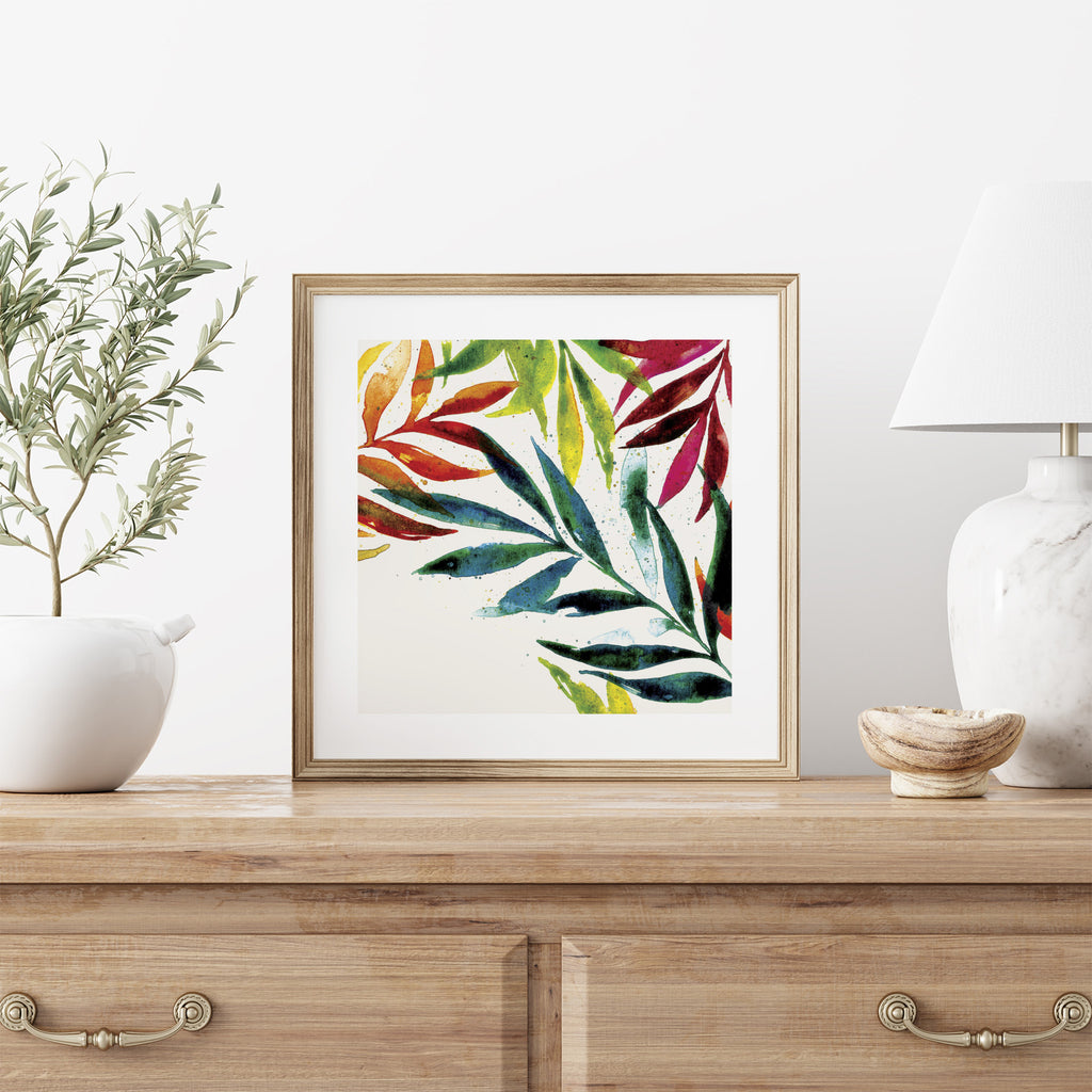 A watercolour art print of colourful leaves. Art print is framed and sits on a dresser.