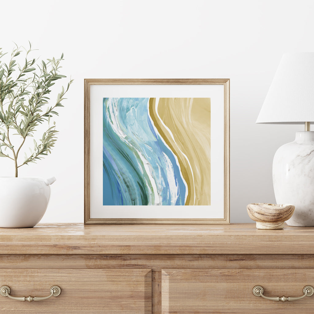 Art print featuring a watercolour scene of waves next to a beach. Art print is stood on a dresser.