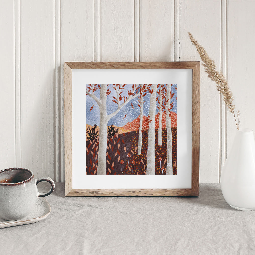 Art print of an Autumnal forest on a clear blue day. Art print is leaning against a white wall.