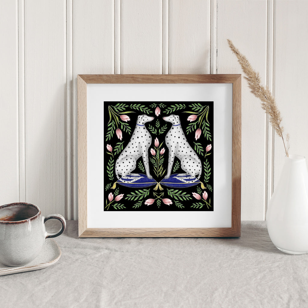 Art print features a detailed illustration of symmetrical spotted dogs surrounded by pink tulips. Art print is sat on a table leaning against a white wall.