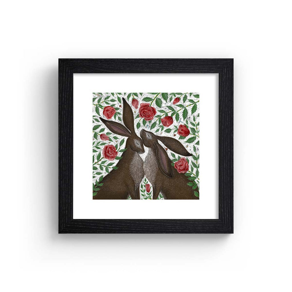 art print features two hares standing in a patch of blooming roses, in a black frame.