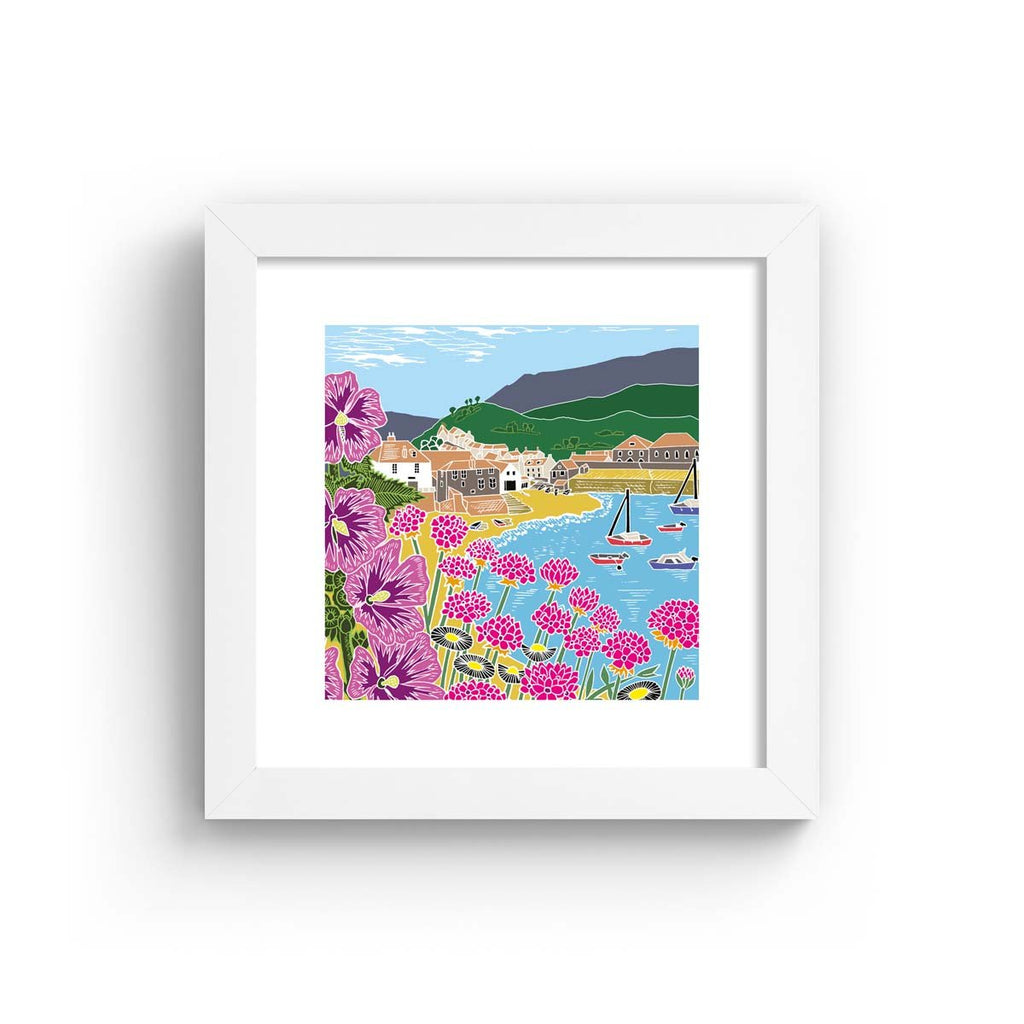 Colourful nature art print featuring a coastal scene of a seaside town, the beach and blooming botanicals. Art print is in a white frame.
