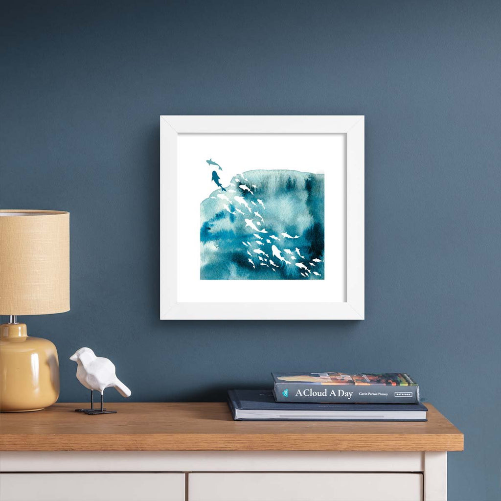 Vibrant watercolour art print featuring the silhouettes of fishes swimming in the ocean. Art print is hung up on a blue wall.