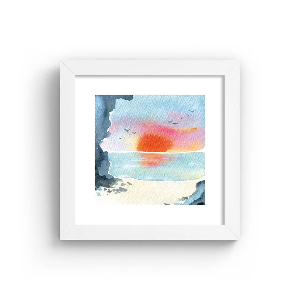 Vibrant watercolour art print featuring a sunset over a coastal scene. Art print is in a white frame.