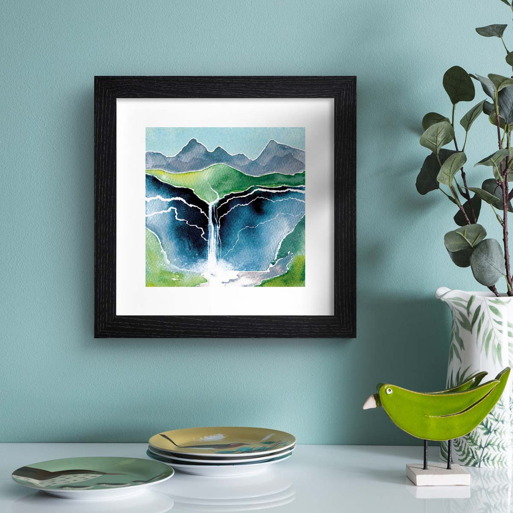 Beautiful watercolour art print featuring a waterfall flowing down a beautiful mountain landscape. Art print is hung up on a blue wall.