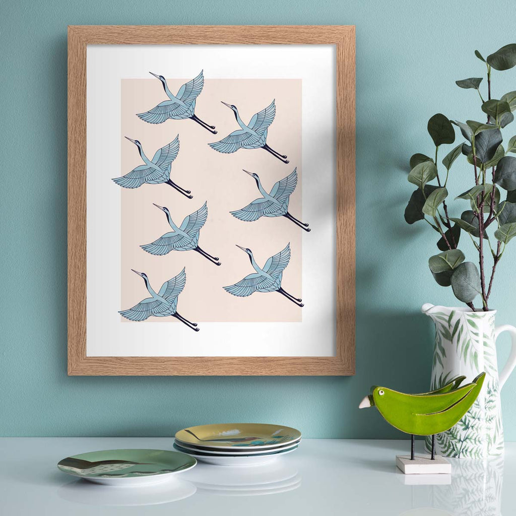 Detailed art print featuring a pattern of heron's flying in formation, on a pale pink background. Art print is hung up on a blue wall.