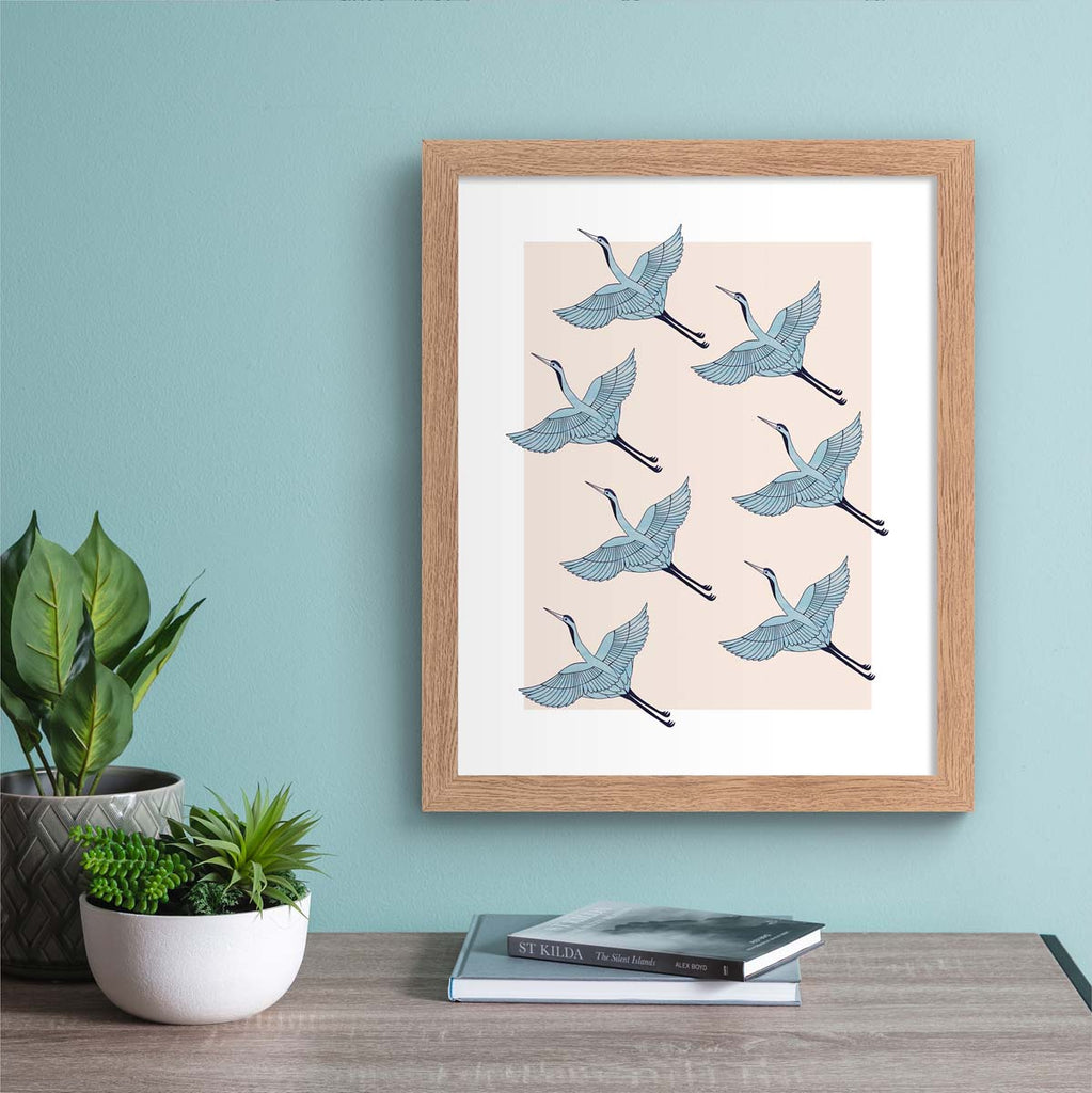 Detailed art print featuring a pattern of heron's flying in formation, on a pale pink background. Art print is hung up on a pale blue wall.