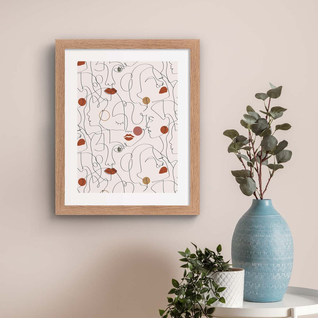 Pastel art print featuring clever line work to create a pleasing pattern of faces. Pink and beige colours are used to emphasise lips and cheeks. Art print is hung up on a pale beige wall.