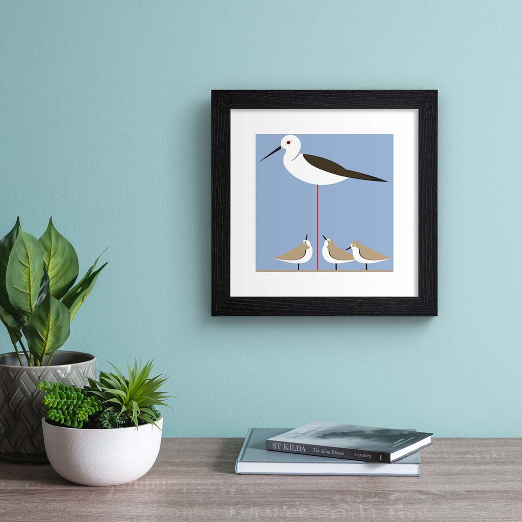 Minimalistic art print featuring small birds perched underneath a tall stilt. Art print is hung up on a blue wall.