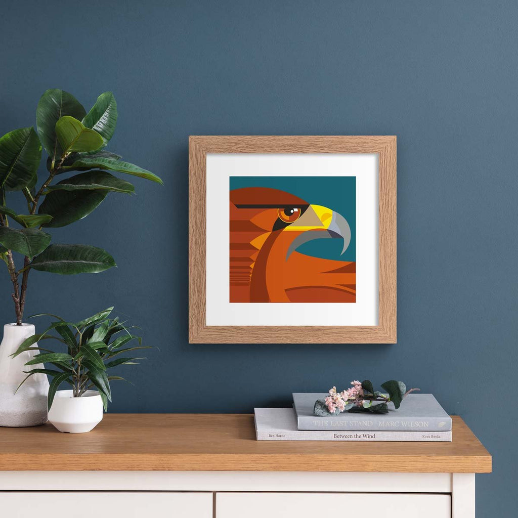 Minimalistic art print featuring a fierce golden eagle in front of a deep blue background. Art print is hung up on a dark blue wall.