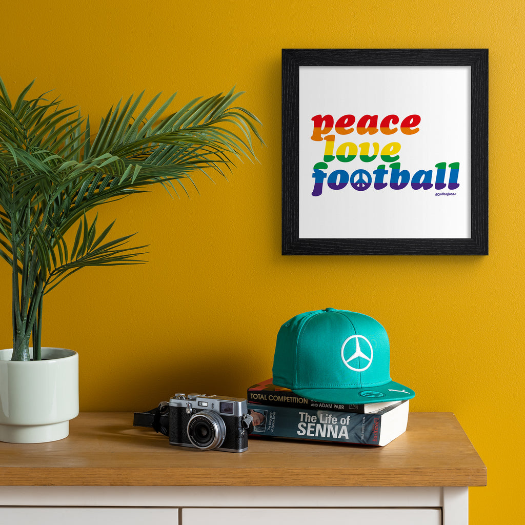 Sporty typography art print celebrating football, stating 'peace, love, football' in multicoloured text. Art print is hung up on an orange wall.