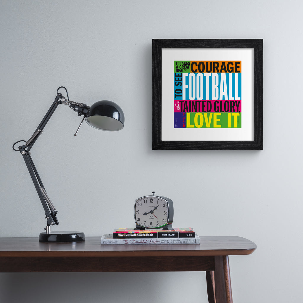 Typography art print celebrating football, on a neon, multicolour background. Typography reads 'It Takes A Great Deal Of Courage To See Football In All Its Tainted Glory, And Still To Love It'. Art print is hung up on a grey wall.
