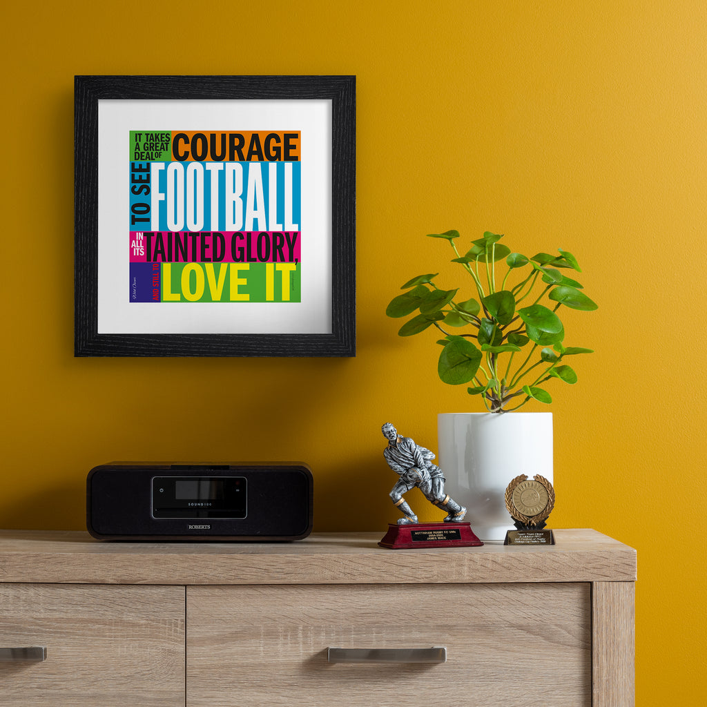 Typography art print celebrating football, on a neon, multicolour background. Typography reads 'It Takes A Great Deal Of Courage To See Football In All Its Tainted Glory, And Still To Love It'. Art print is hung up on an orange wall.