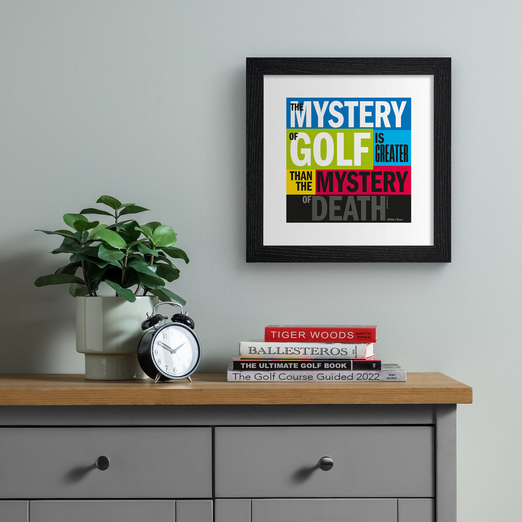 This vibrant typography art print celebrates golf, on a bright multicoloured background. Typography states 'The Mystery Of Gold Is Greater Than The Mystery Of Death'. Art print is hung up on a grey wall.