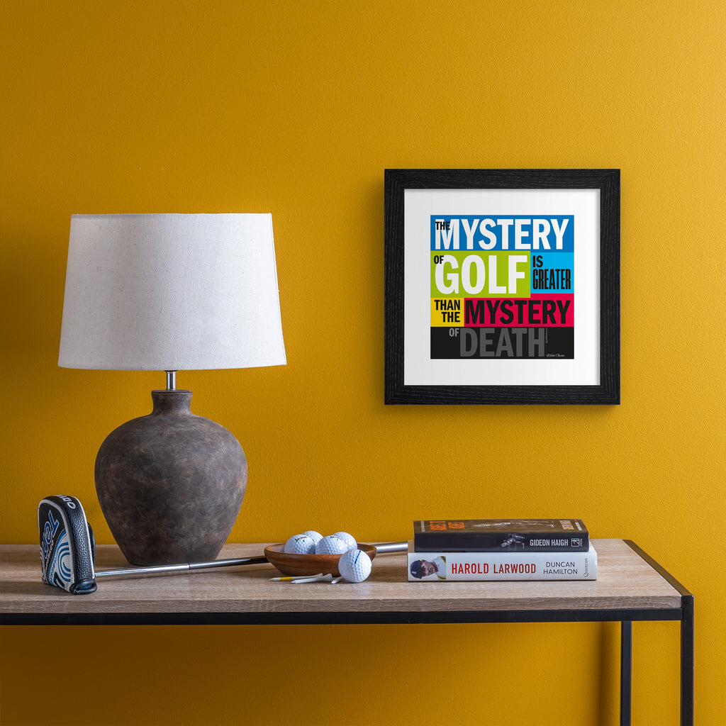 This vibrant typography art print celebrates golf, on a bright multicoloured background. Typography states 'The Mystery Of Gold Is Greater Than The Mystery Of Death'. Art print is hung up on an orange wall.