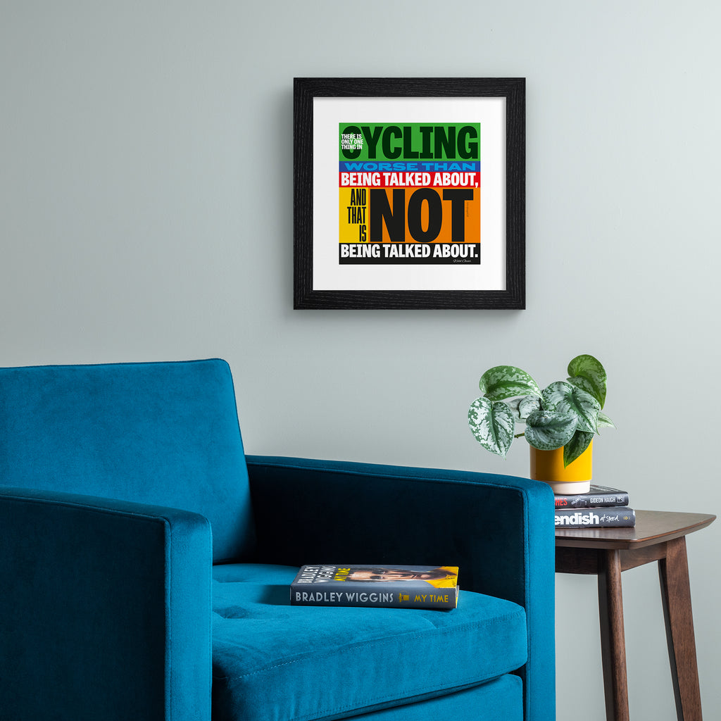 Sporty art print featuring typography celebrating cycling, on a multicolour background. Typography reads 'There Is Only One Thing In Cycling Worse Than Being Talked About, And That Is Not Being Talked About.' Art print is hung up on a grey wall.