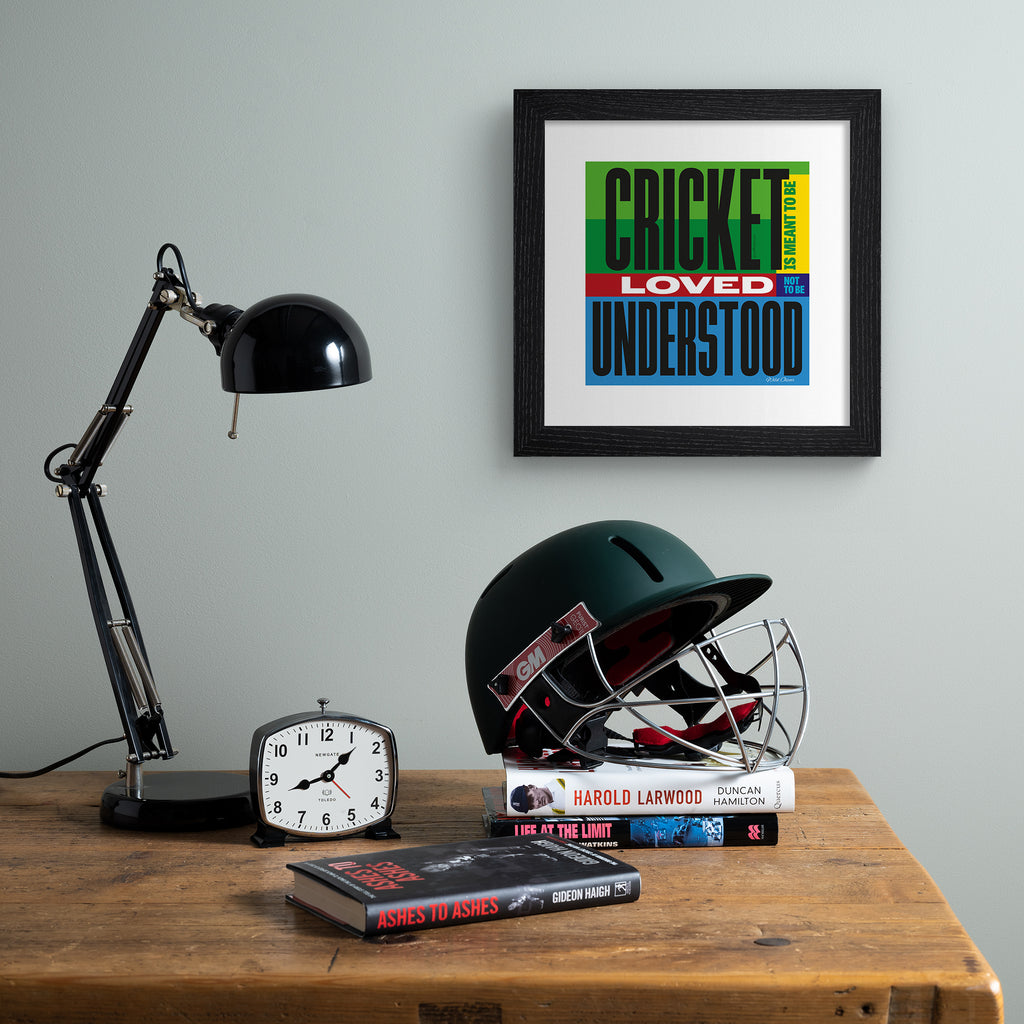Typography art print celebrating cricket, on a bright green, blue, yellow and red background. Typography reads 'Cricket Is Meant To be Loved, Not To Be Understood'. Art print is hung up on a grey wall.