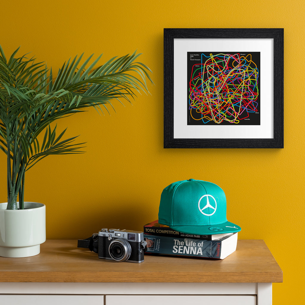 Sports art print celebrating Lewis Hamilton, featuring brightly coloured lines in a pattern on a dark background.  Art print is hung up on an orange wall.