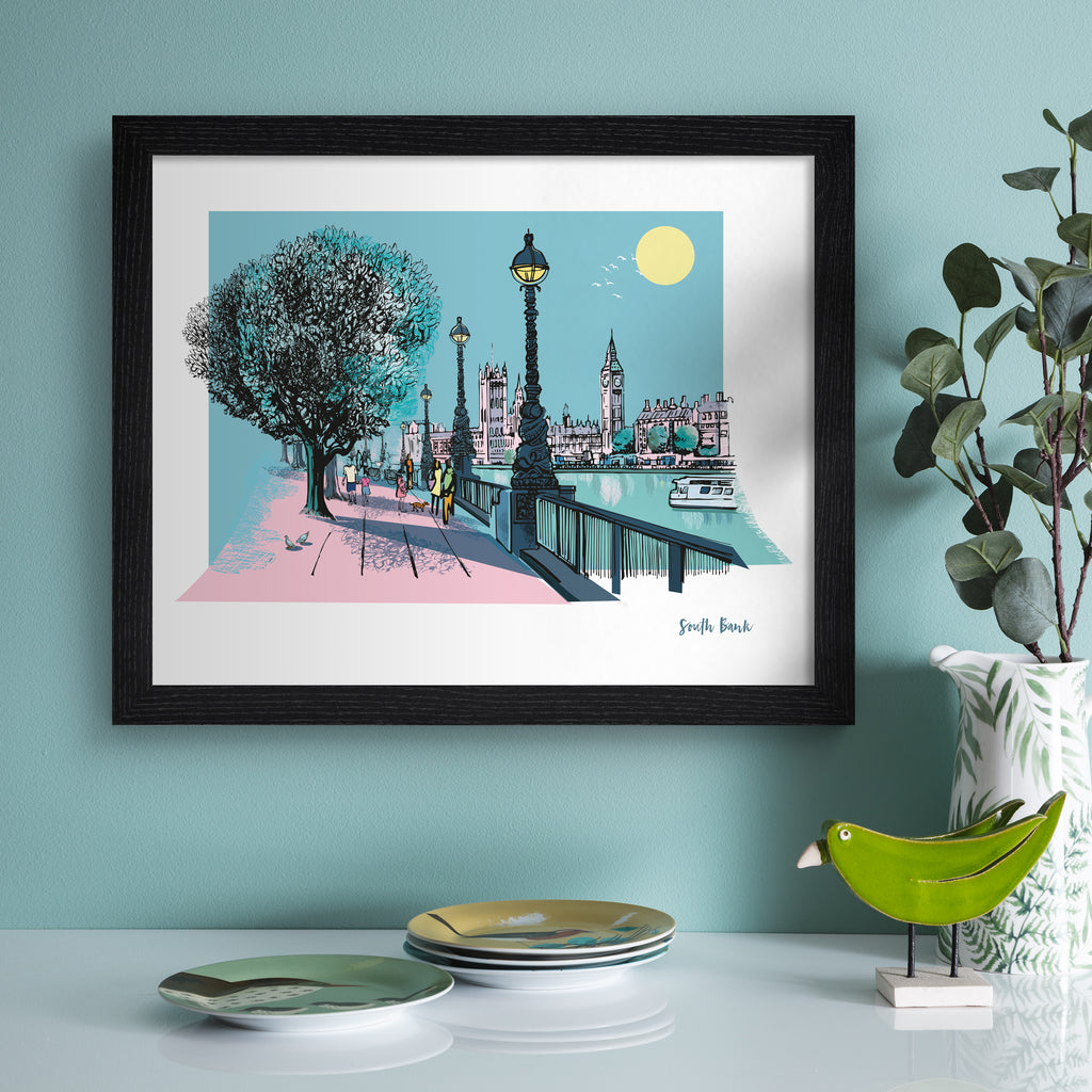 Vivid travel art print featuring South Bank in London, in vivid pastel colours. Title in the bottom right hand corner reads 'South Bank'. Art print is hung up on a blue wall.