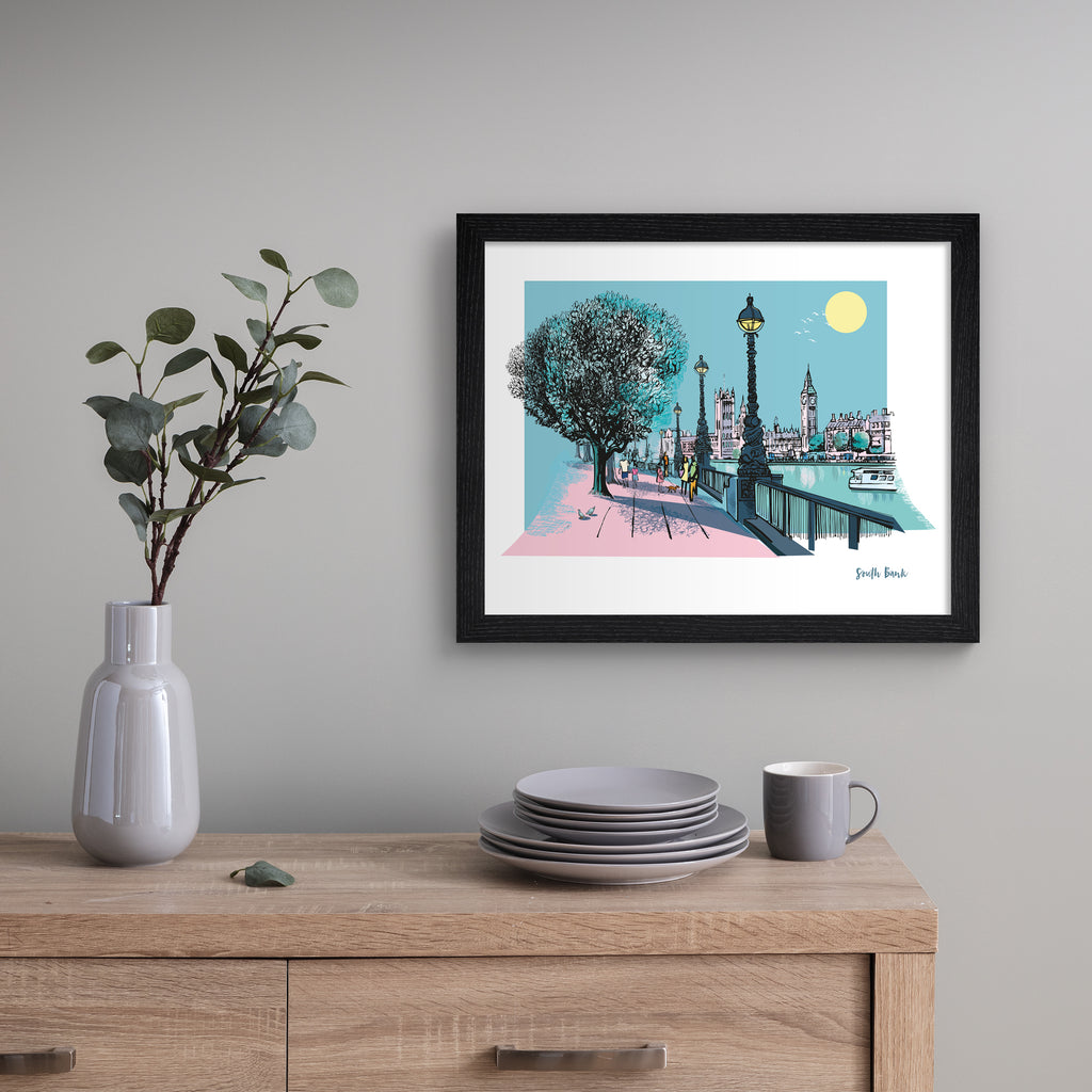 Vivid travel art print featuring South Bank in London, in vivid pastel colours. Title in the bottom right hand corner reads 'South Bank'. Art print is hung up on a grey wall.
