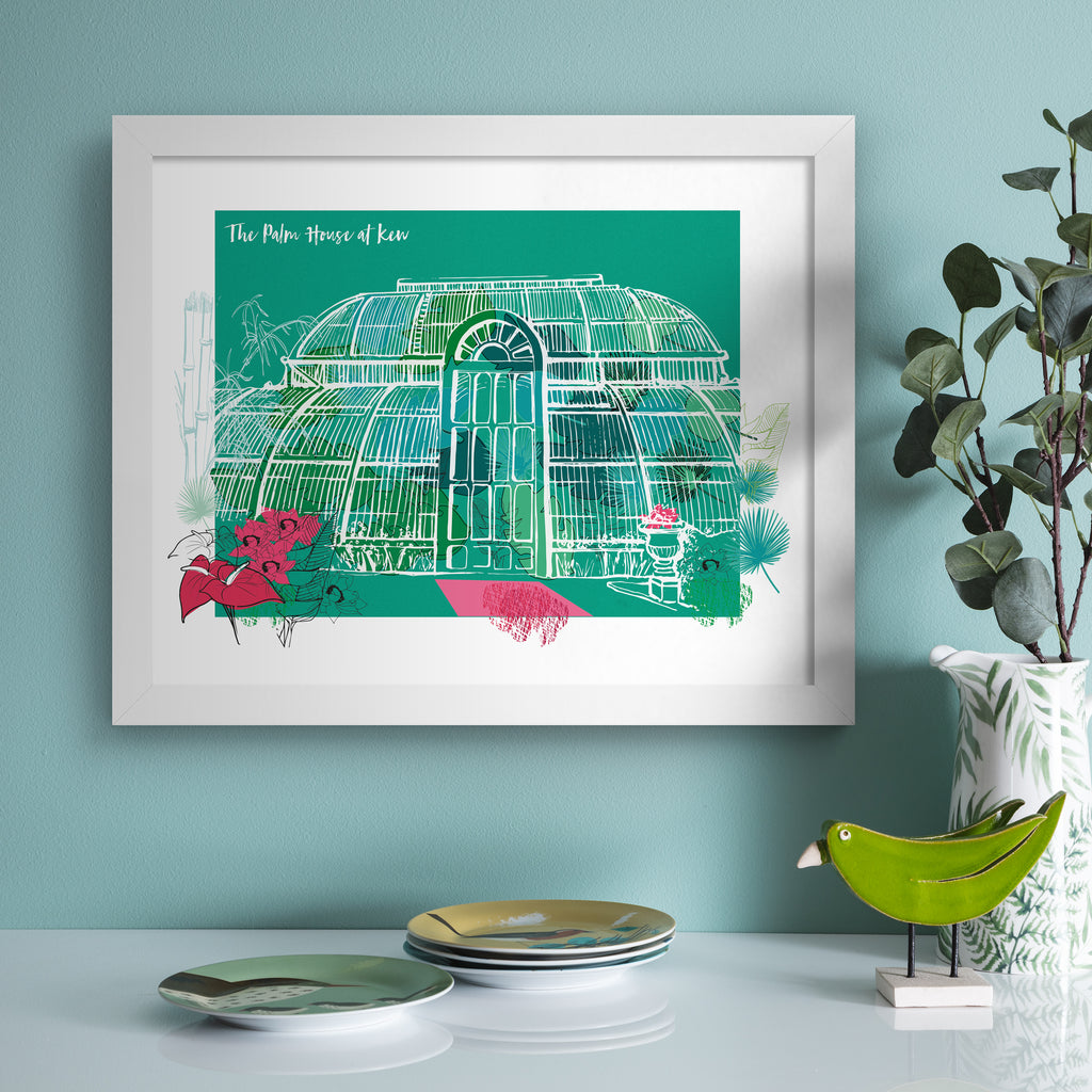 Vibrant travel art print featuring The Palm House At Kew Gardens in London, bordered by bright blooming flowers, on a green background. Title at the top left reads 'The Palm House At Kew'. Art print is hung up on a blue wall.