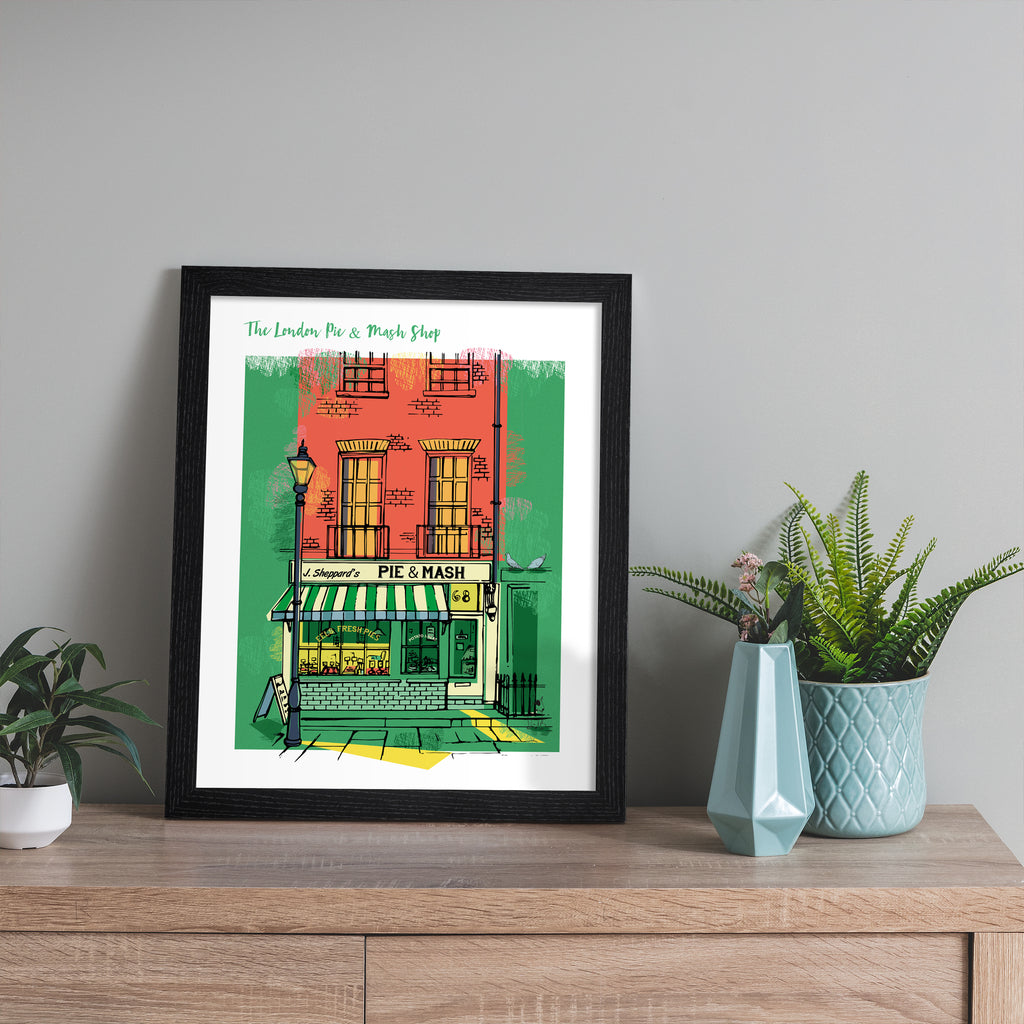 Vibrant travel art print featuring the London Pie & Mash Shop, amidst a bright orange and green background. Title at the top reads 'The London Pie & Mash Shop'. Art print is leaning against a grey wall.