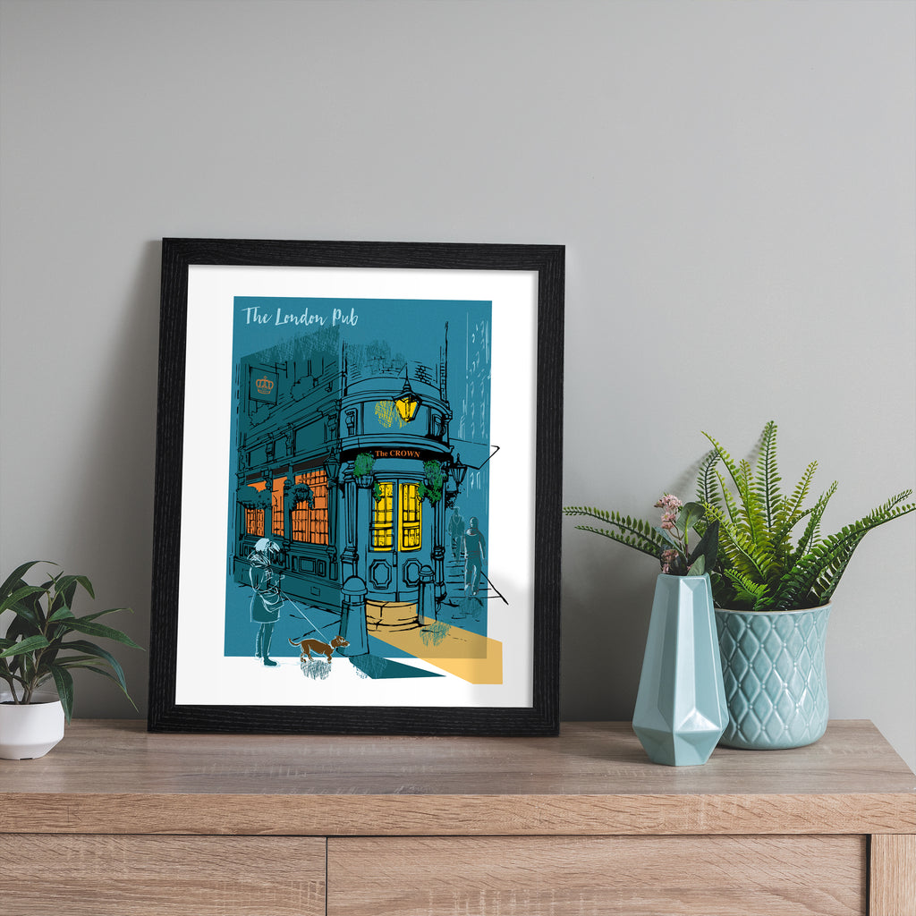 Vibrant travel art print featuring The London Pub, bathed in a dark blue and amber background. Title at the top reads 'The London Pub'. Art print is leaning against a beige wall.
