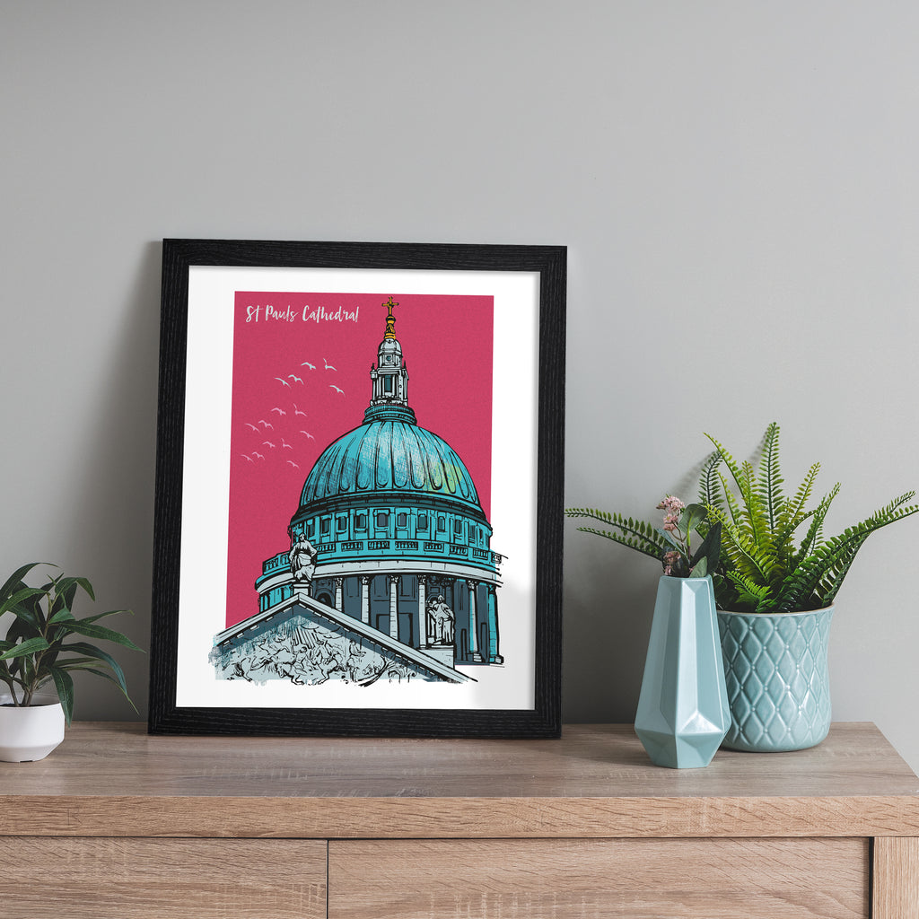 Vibrant travel art print featuring St Paul's Cathedral in London, amidst a bright pink background. Title in top left corner reads 'St Paul's Cathedral'.  Art print is leaning against a grey wall.