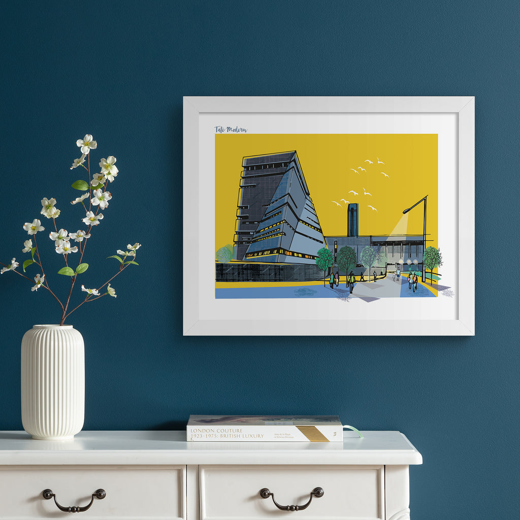 Colourful travel art print featuring a detailed illustration of the Tate Modern in London, in front of a vibrant yellow background. Title in the top left corner reads 'Tate Modern'. Art print is hung up on a dark blue wall.