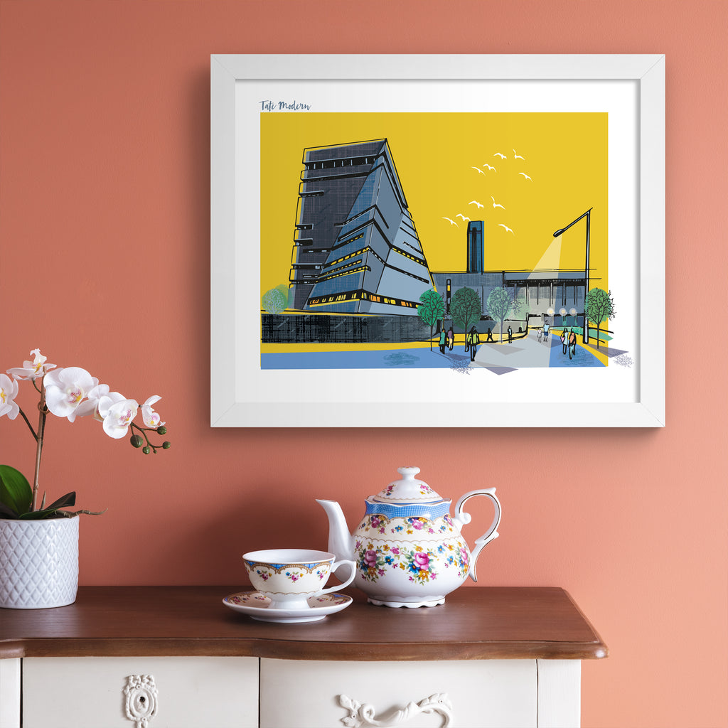 Colourful travel art print featuring a detailed illustration of the Tate Modern in London, in front of a vibrant yellow background. Title in the top left corner reads 'Tate Modern'. Art print is hung up on a pink wall.