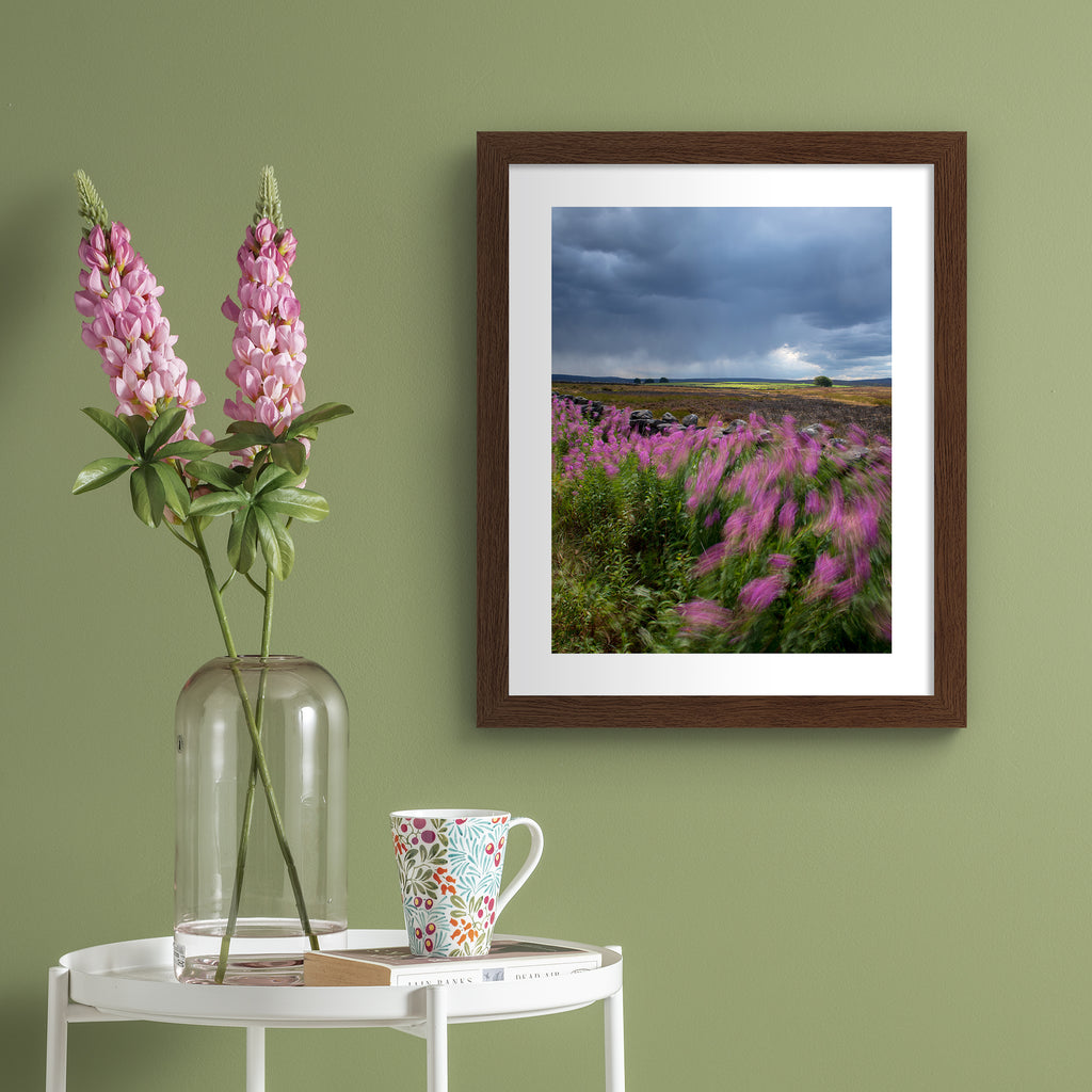 Beautiful photography art print featuring a windy field of beautiful flowers under a moody sky. Art print is hung up on a green wall.