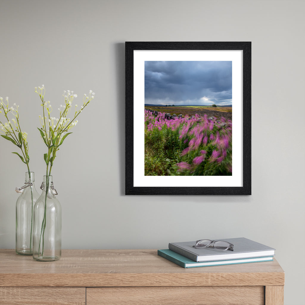 Beautiful photography art print featuring a windy field of beautiful flowers under a moody sky. Art print is hung up on a grey wall.