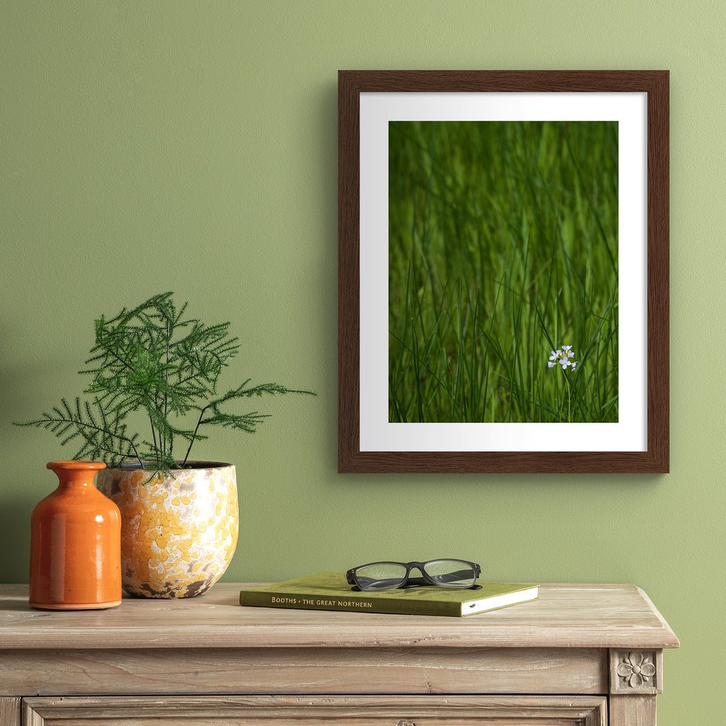 Beautiful photography art print featuring a vivid green field with a bright white flower nestled in the bottom corner. Art print is hung up on a green wall.