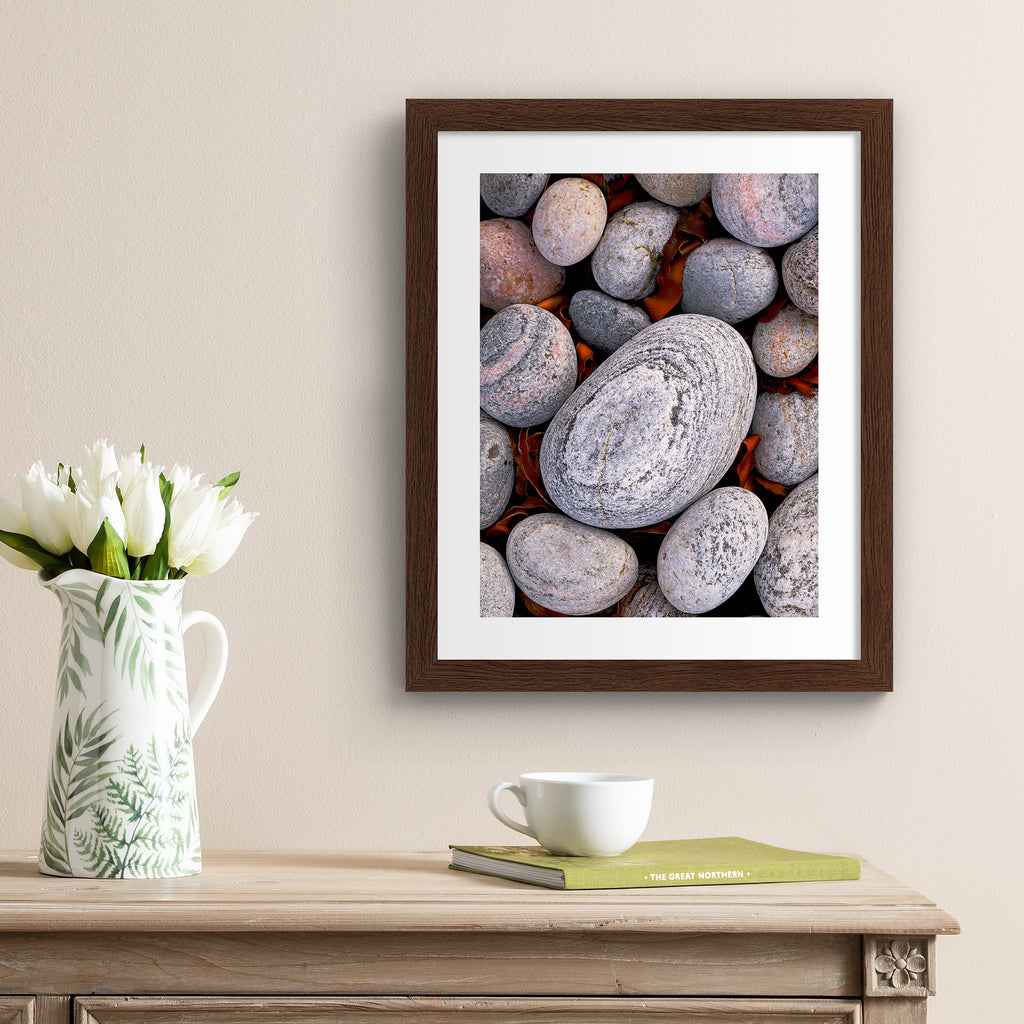 Beautifully simplistic photography art print featuring a close of up of pebbles found on a beach. Art print is hung up on a pale beige wall.