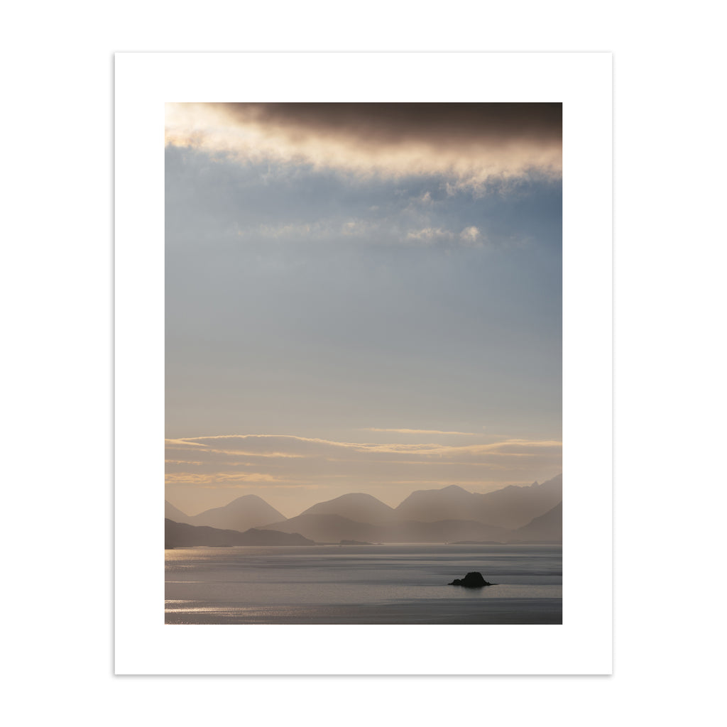 Emotive photography art print featuring a sweeping scene of the Isle of Sky, including shimmering water, a warm sunrise and moody cliffs in the distance. 