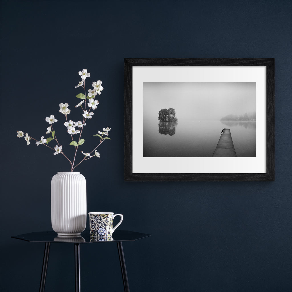 Moody black and white photography art print featuring mist flowing over still waters. Art print is hung up on a dark blue wall.